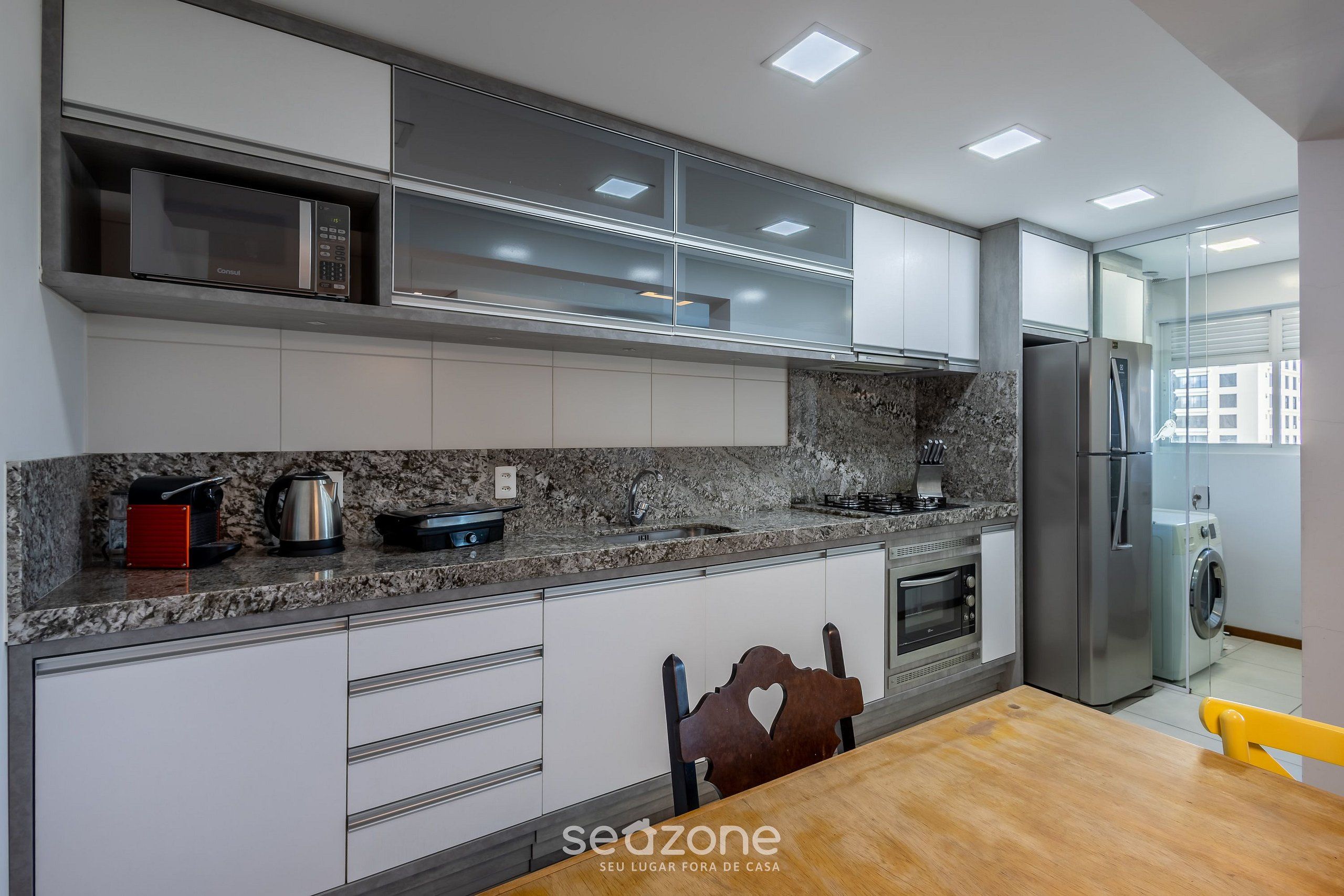Una cocina moderna con electrodomésticos integrados, encimera de granito y comedor con mesa y sillas de madera.