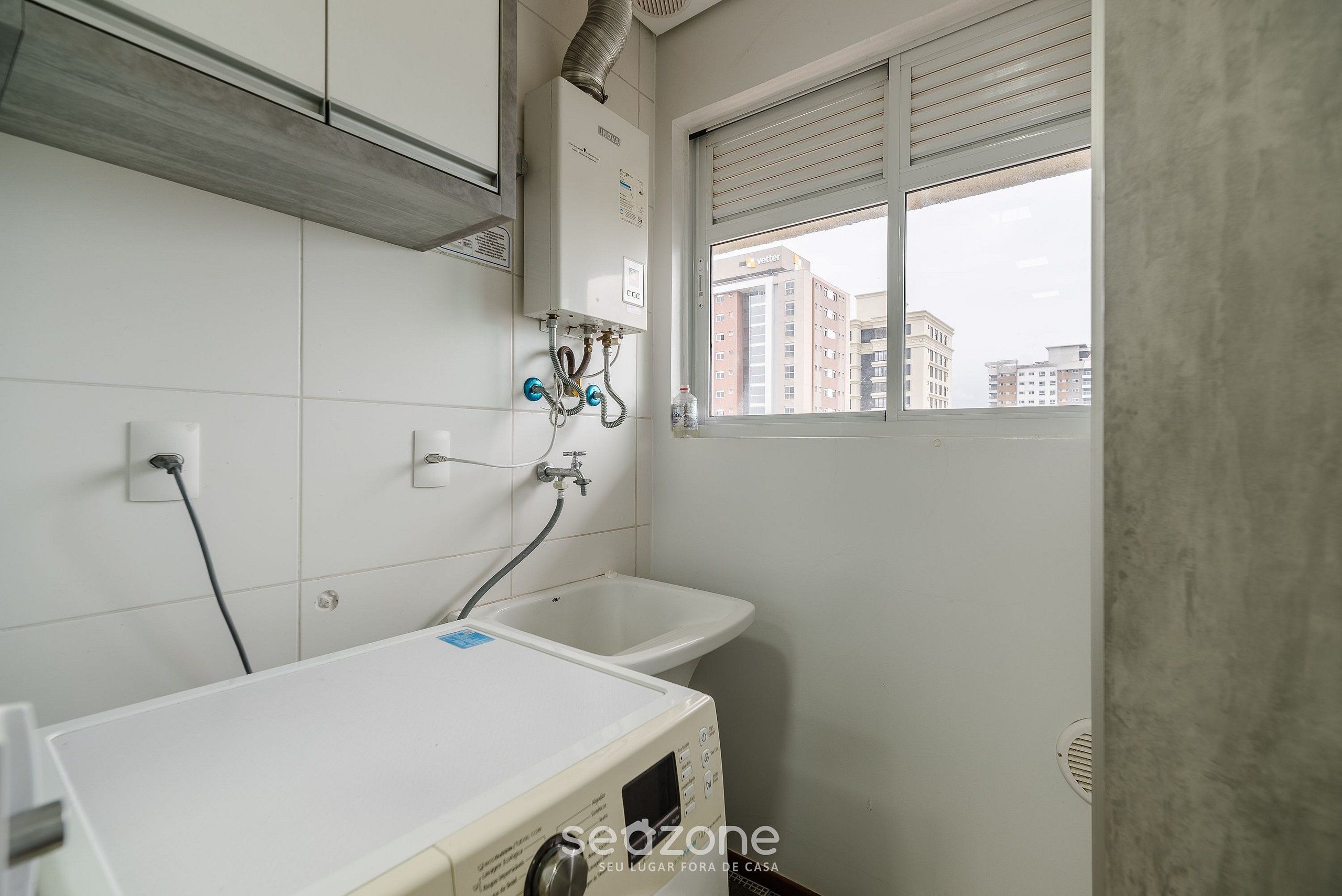 A bathroom with a white sink, a window with a view of buildings, and a heater on the wall.