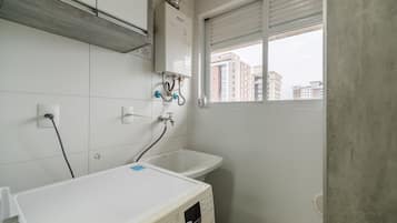 A bathroom with a white sink, a window with a view of buildings, and a heater on the wall.