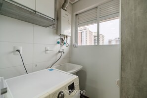 A bathroom with a white sink, a window with a view of buildings, and a heater on the wall. - Apto Vista Mar com churrasqueira BBH1003 (Picarras)