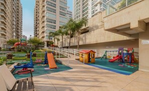 A playground with slides and climbing structures, surrounded by high-rise buildings. - Apto Vista Mar com churrasqueira BBH1003 (Picarras)