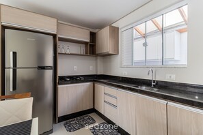 Une cuisine moderne dotée d’un réfrigérateur en acier inoxydable, de meubles en bois, d’un plan de travail noir et d’une fenêtre avec un puits de lumière.