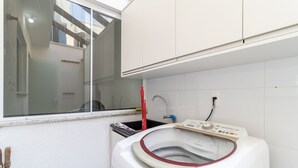 Un lavadero pequeño y funcional con lavadora de carga frontal, una ventana y un lavamanos.