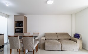 Een moderne woonkamer met een beige bank, een eettafel met stoelen en inbouwmeubels.