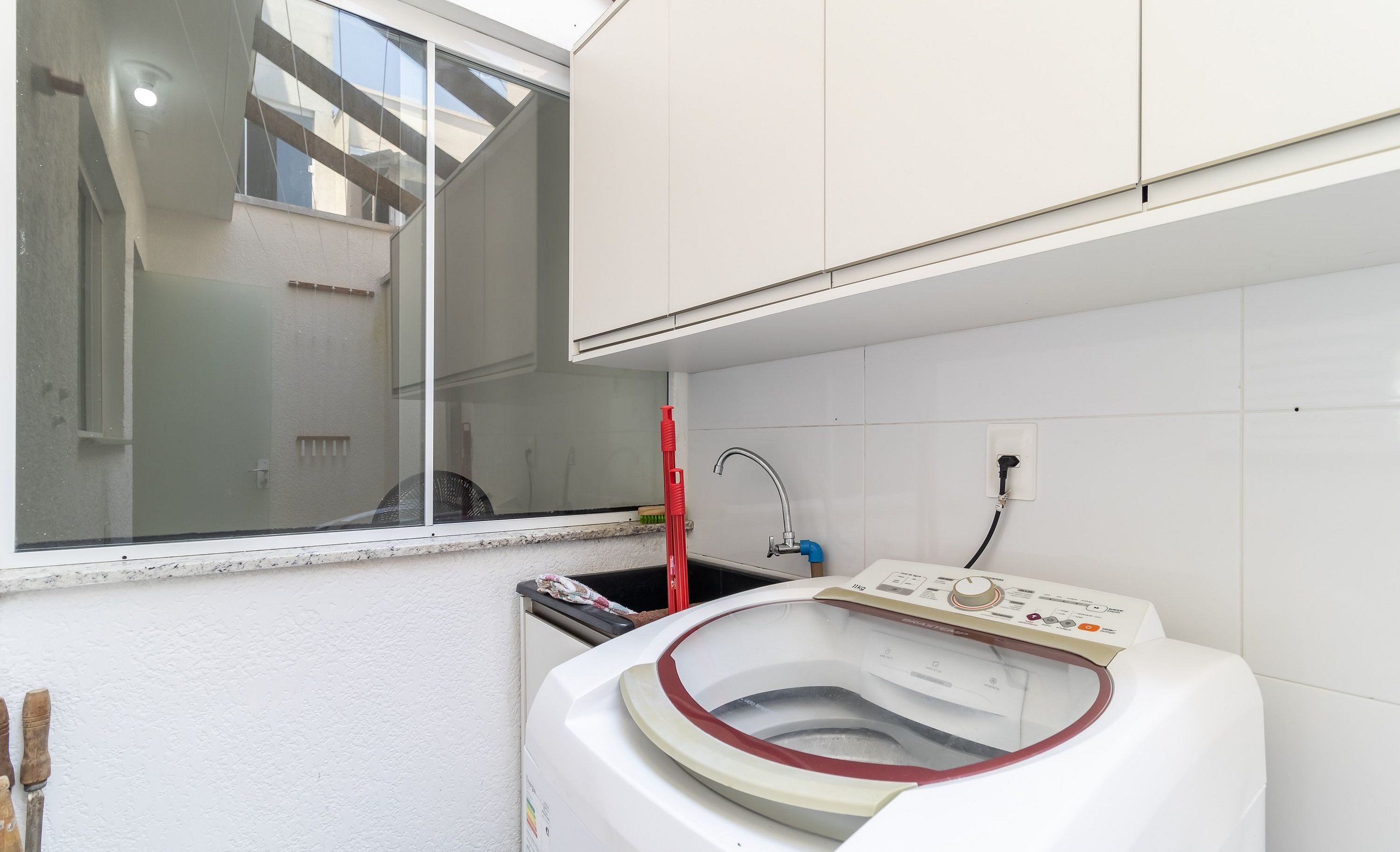 A compact laundry room with a front-loading washing machine, a window, and a small sink.