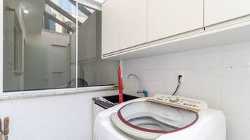 A compact laundry room with a front-loading washing machine, a window, and a small sink.