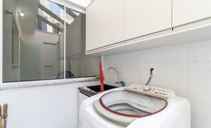 A compact laundry room with a front-loading washing machine, a window, and a small sink.