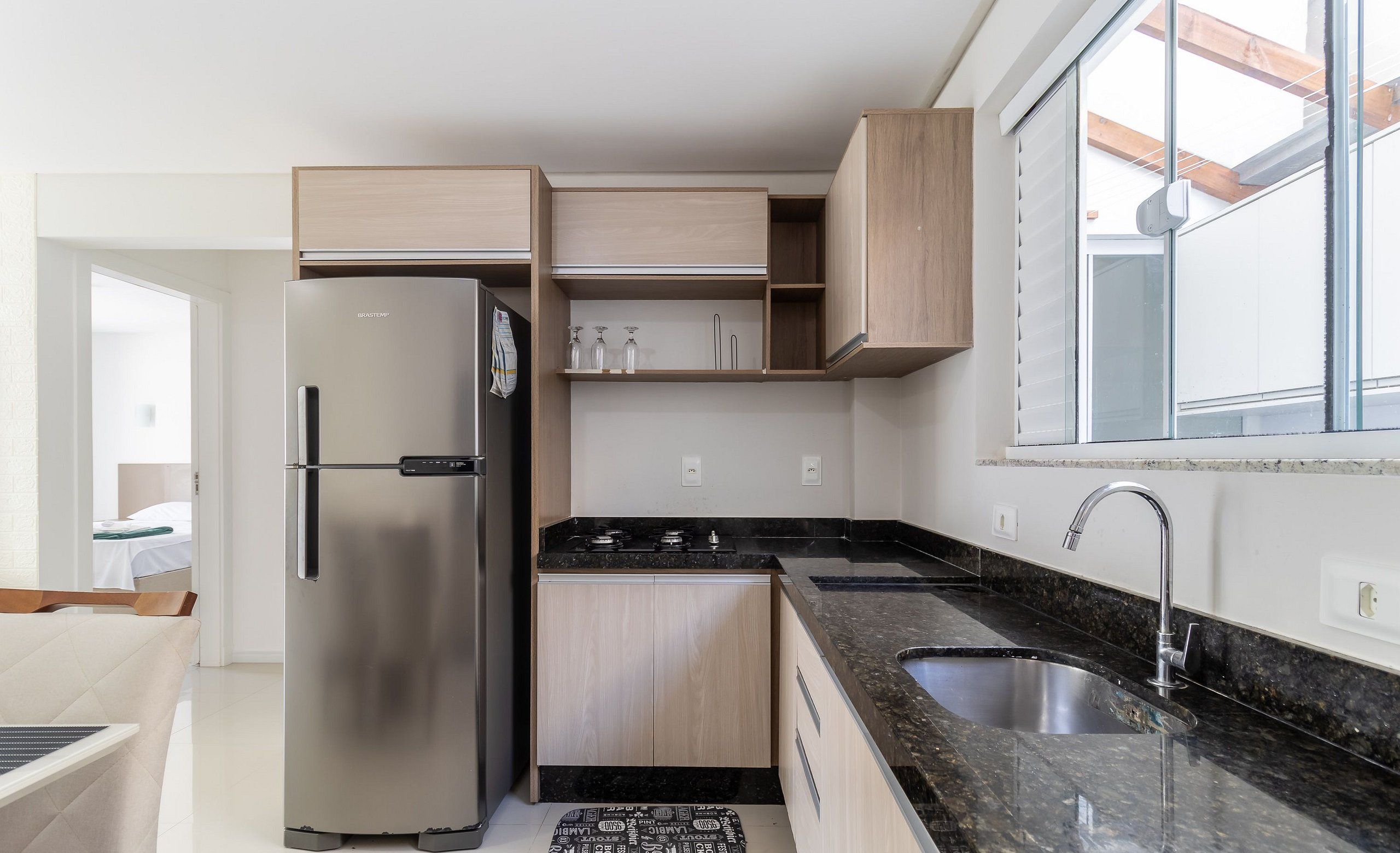 A modern kitchen with a stainless steel refrigerator, wooden cabinets, a granite countertop, and a window with a view.