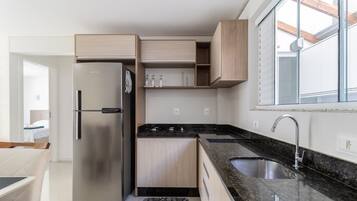 A modern kitchen with a stainless steel refrigerator, wooden cabinets, a granite countertop, and a window with a view.