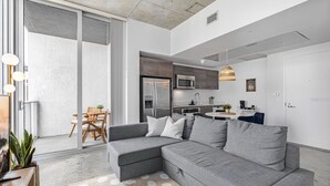 En moderne stue med en grå hjørnesofa, et spiseområde med et træbord og stole, og et køkken med rustfrie stålemmer.