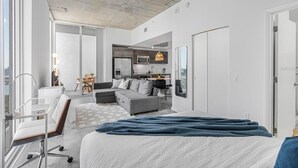 Et moderne hotelværelse med en stor seng, et skrivebord med stol, en sofa, et spiseområde og et tekøkken.
