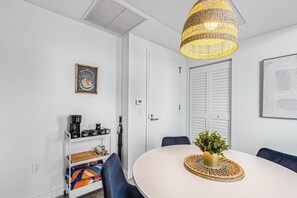 Una habitación moderna y bien iluminada con una mesa redonda, una lámpara colgante de mimbre, una estación de café y un cuadro en la pared.