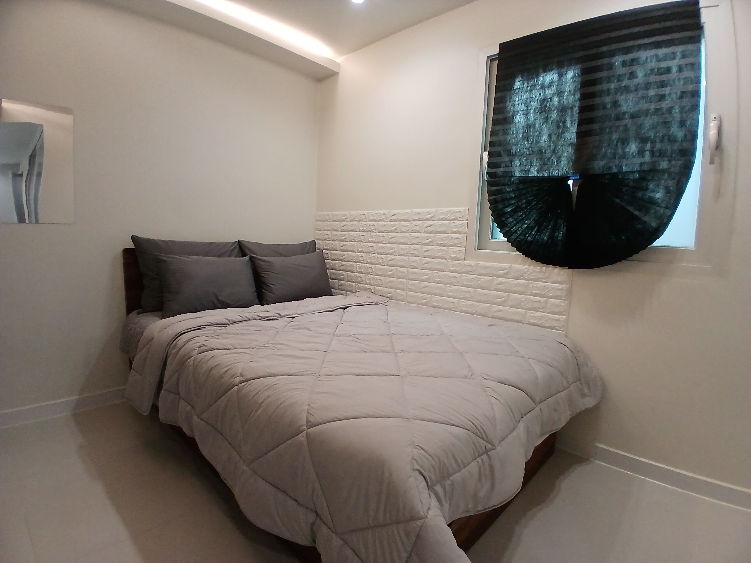 A bedroom with a bed, a window with a curtain, and a textured wall.