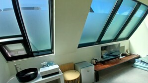 Cocina moderna con lavamanos, estufa y un refrigerador pequeño. Amplias ventanas ofrecen luz natural y vistas del cielo.
