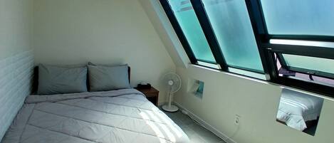 A bedroom with a bed, a nightstand, a wall-mounted fan, and a skylight.