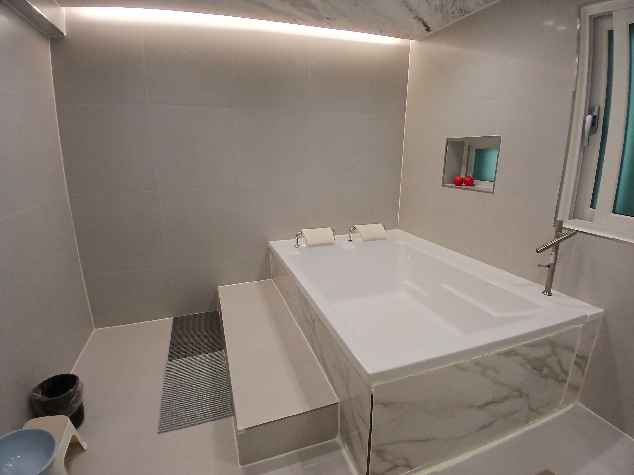 A modern bathroom with a large rectangular bathtub, a small window with a view, and a tiled floor.