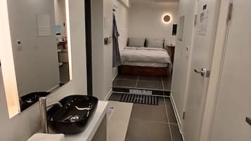 A modern hotel room with a large mirror, a black sink, a bed, and a small rug.