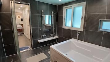 A modern bathroom with a large bathtub, a shower area, and a vanity with a mirror.