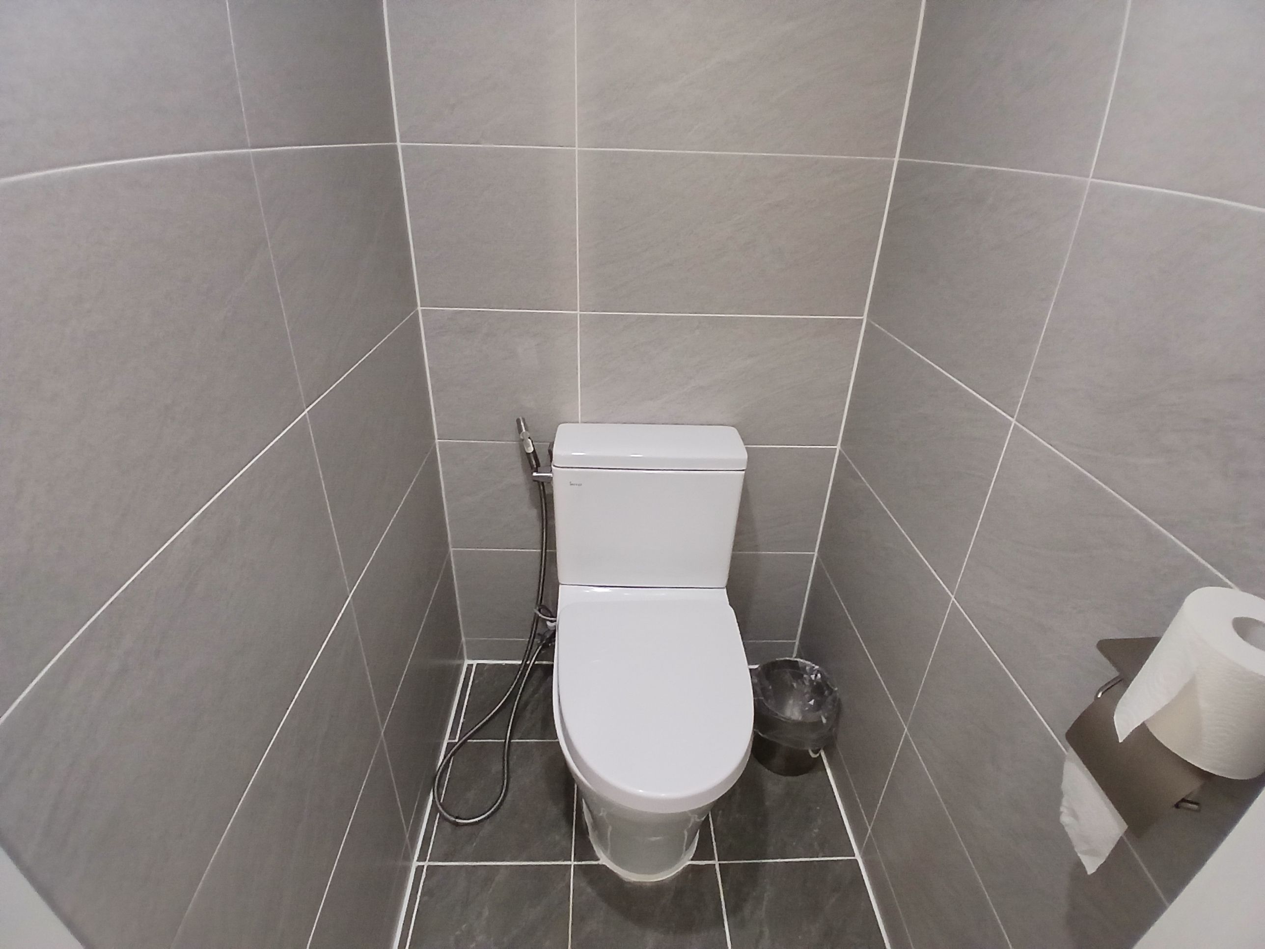 A small, modern bathroom with a toilet, bidet, and a paper towel dispenser.