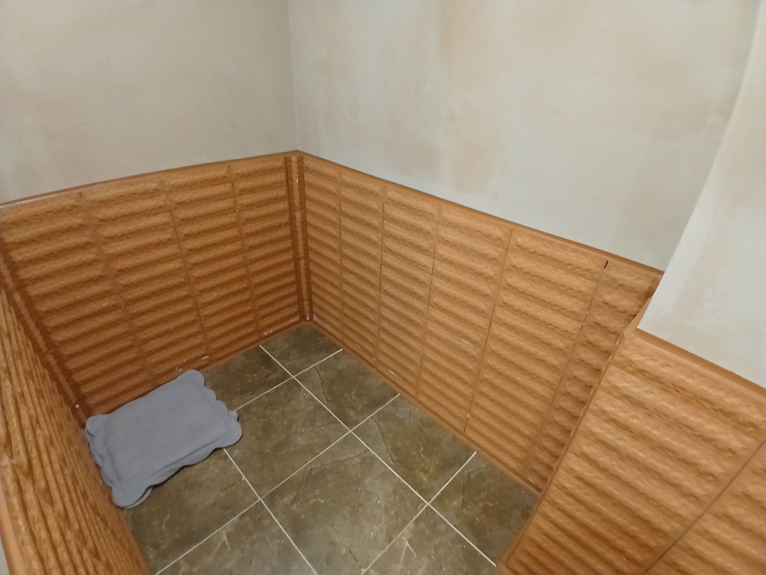 A corner of a room with tiled flooring and wooden paneling on the walls.