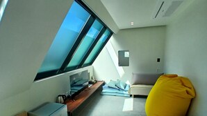 Una habitación moderna y funcional con tragaluz, una cama, un escritorio y un pequeño espacio de descanso.