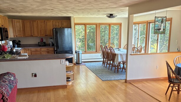 A spacious kitchen with wooden cabinets, a large island, and a dining area with a view of trees through large windows. - Winter deal! Delightful 3-4 bed one floor, 3 baths, fireplace  (Essex)