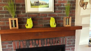 A brick fireplace with a wooden mantel, two potted plants, and a framed picture above it. - Winter deal! Delightful 3-4 bed one floor, 3 baths, fireplace  (Essex)