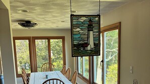A dining area with a table and chairs, large windows with a view of trees, and a hanging light fixture. - Winter deal! Delightful 3-4 bed one floor, 3 baths, fireplace  (Essex)