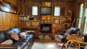 Un intérieur de chalet chaleureux avec un canapé en cuir, des murs en bois, un téléviseur à écran plat et une cheminée.