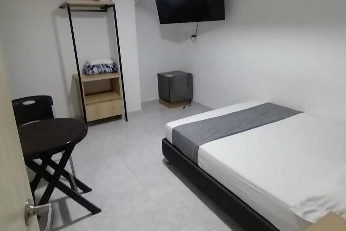 Een kleine, moderne kamer met een bed, een bureau, een stoel, een televisie en een verwarming.