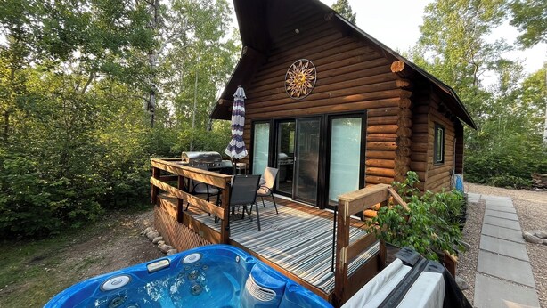 A wooden cabin with a deck, a hot tub, and a patio area with outdoor furniture.