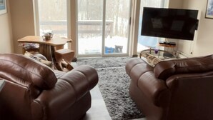 A spacious living room with two brown leather sofas, a flat-screen TV, and a wooden ceiling.