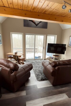 A spacious living room with two brown leather sofas, a flat-screen TV, and a wooden ceiling.