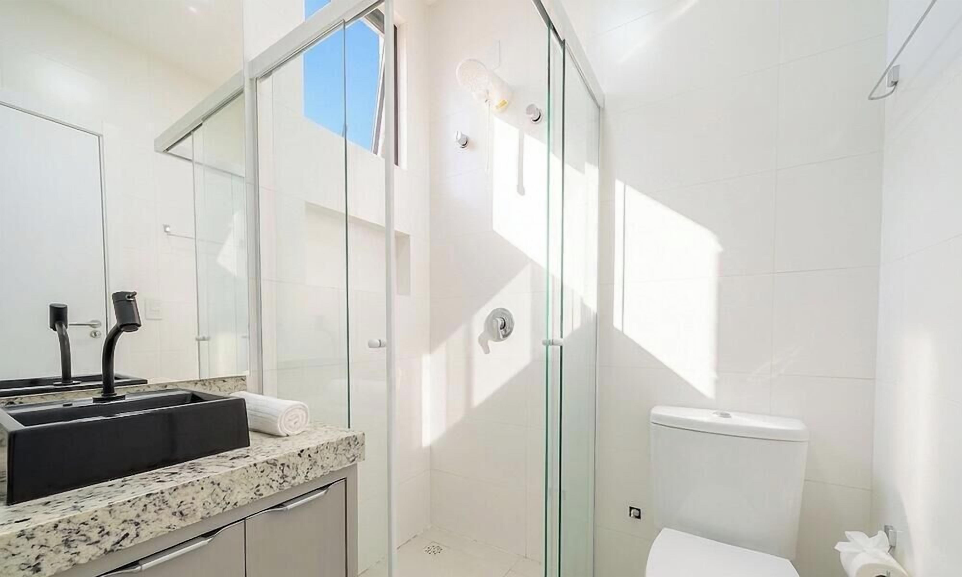 Um banheiro moderno com box de vidro, pia com torneira preta e vaso sanitário.