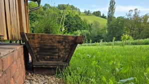 A wooden planter box with a variety of plants, positioned next to a brick wall and a wooden structure.