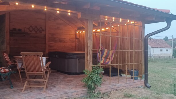 A wooden cabin with a patio area featuring a table and chairs, a hot tub, and string lights.