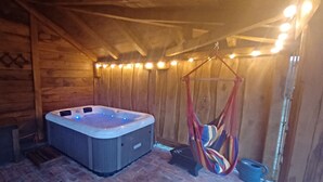 A wooden cabin with a hot tub, a hammock, and a rustic interior.