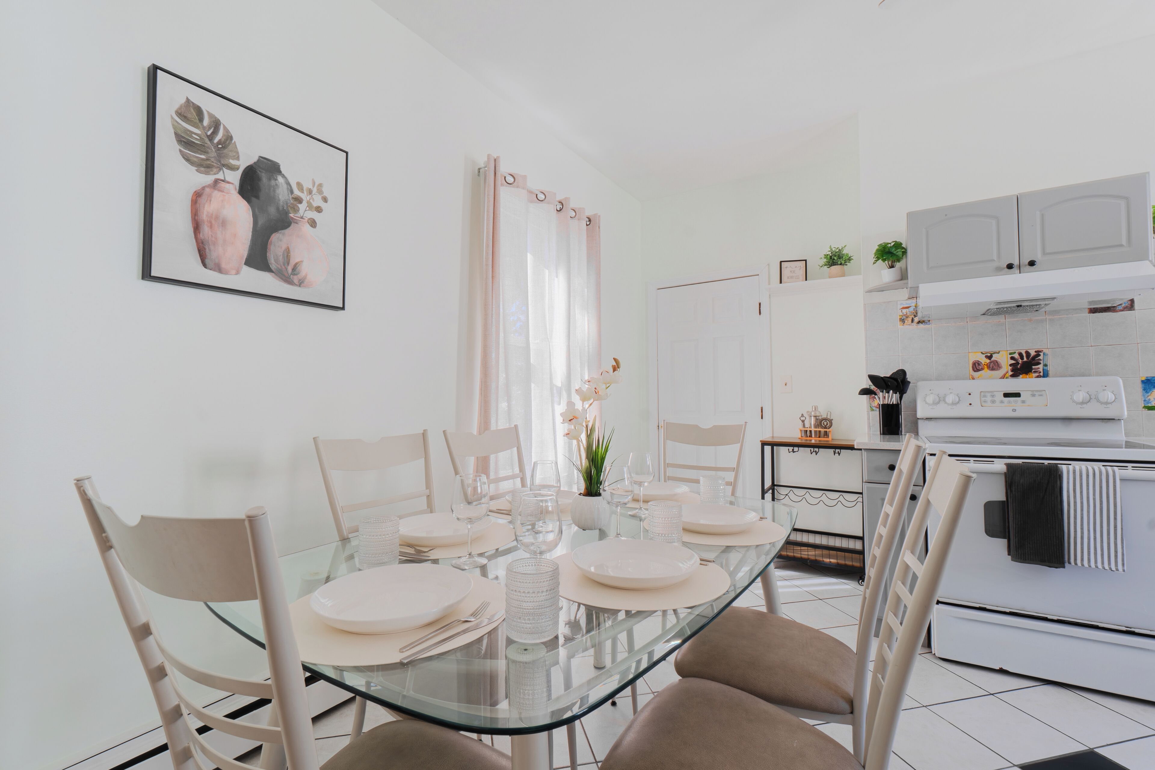 A dining area with a glass table, beige chairs, and a white cabinet in the background.