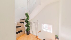 Eine Treppe mit einer spiralförmigen, grünen Pflanze, weißen Geländern und einem kleinen Fenster auf der oberen Plattform.