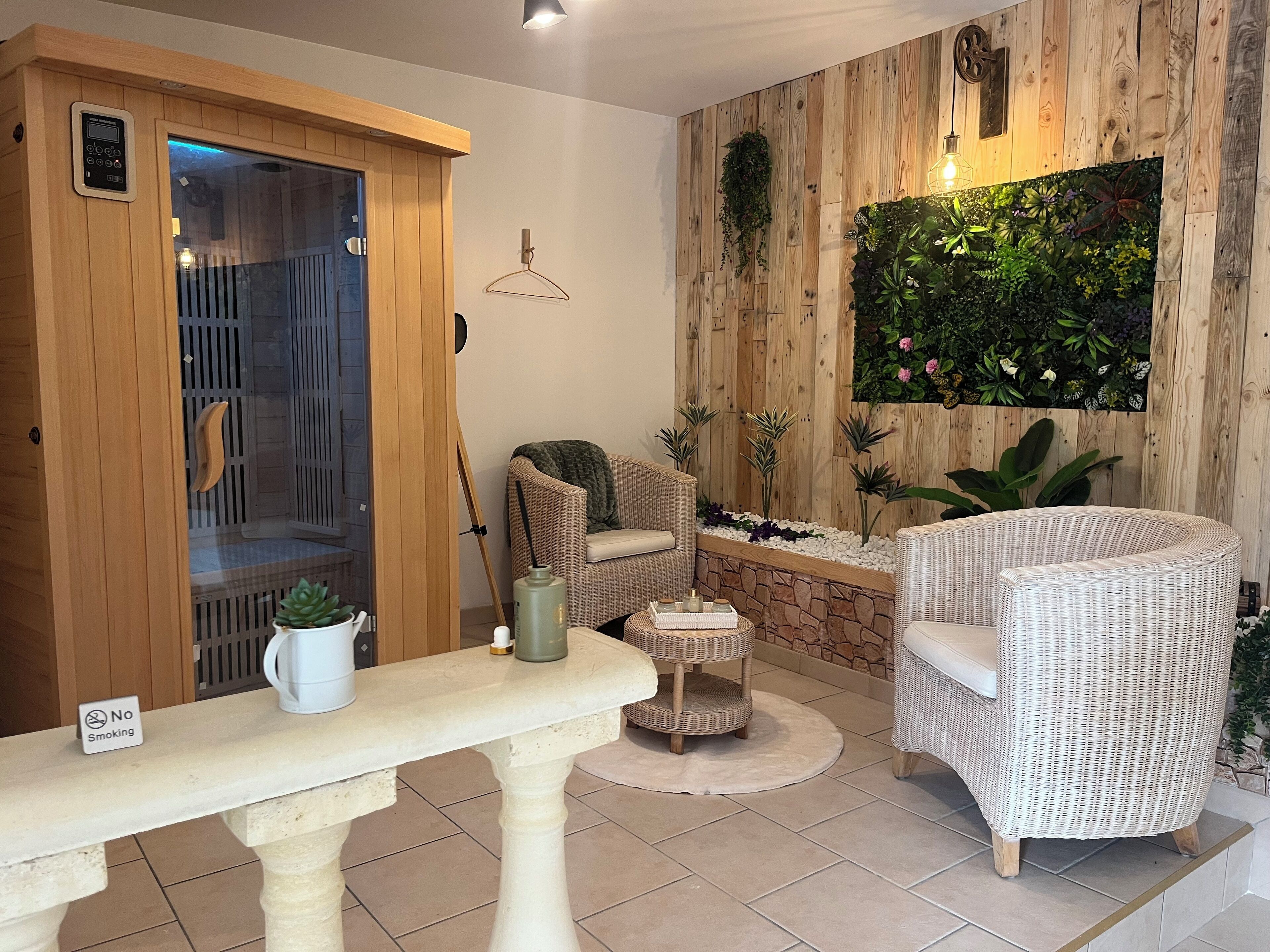 Une pièce avec un sauna, des meubles en osier, un mur de pierre agrémenté de plantes et un panneau indiquant qu'il est interdit de fumer.