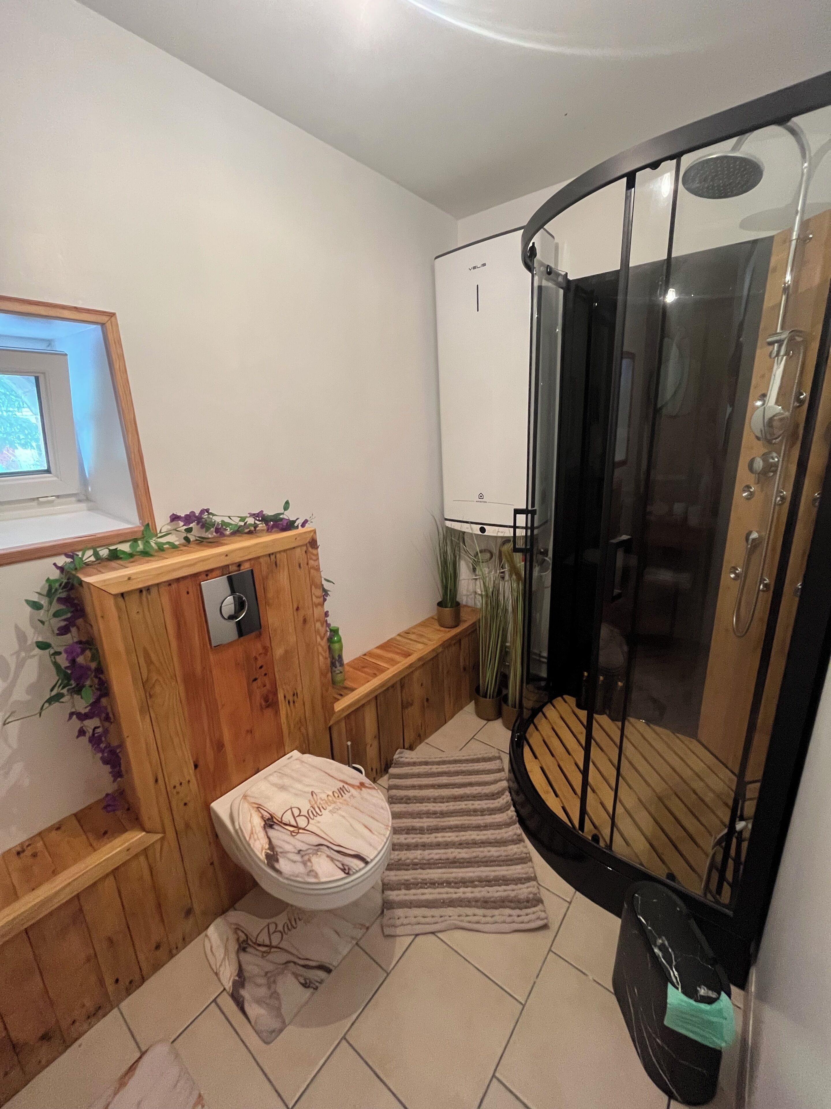 Ein Badezimmer mit Holzwaschtisch, Toilette, Duschkabine und kleinem Fenster.