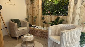 Une pièce chaleureuse avec deux fauteuils en osier, une petite table ronde et un mur décoratif agrémenté de plantes.