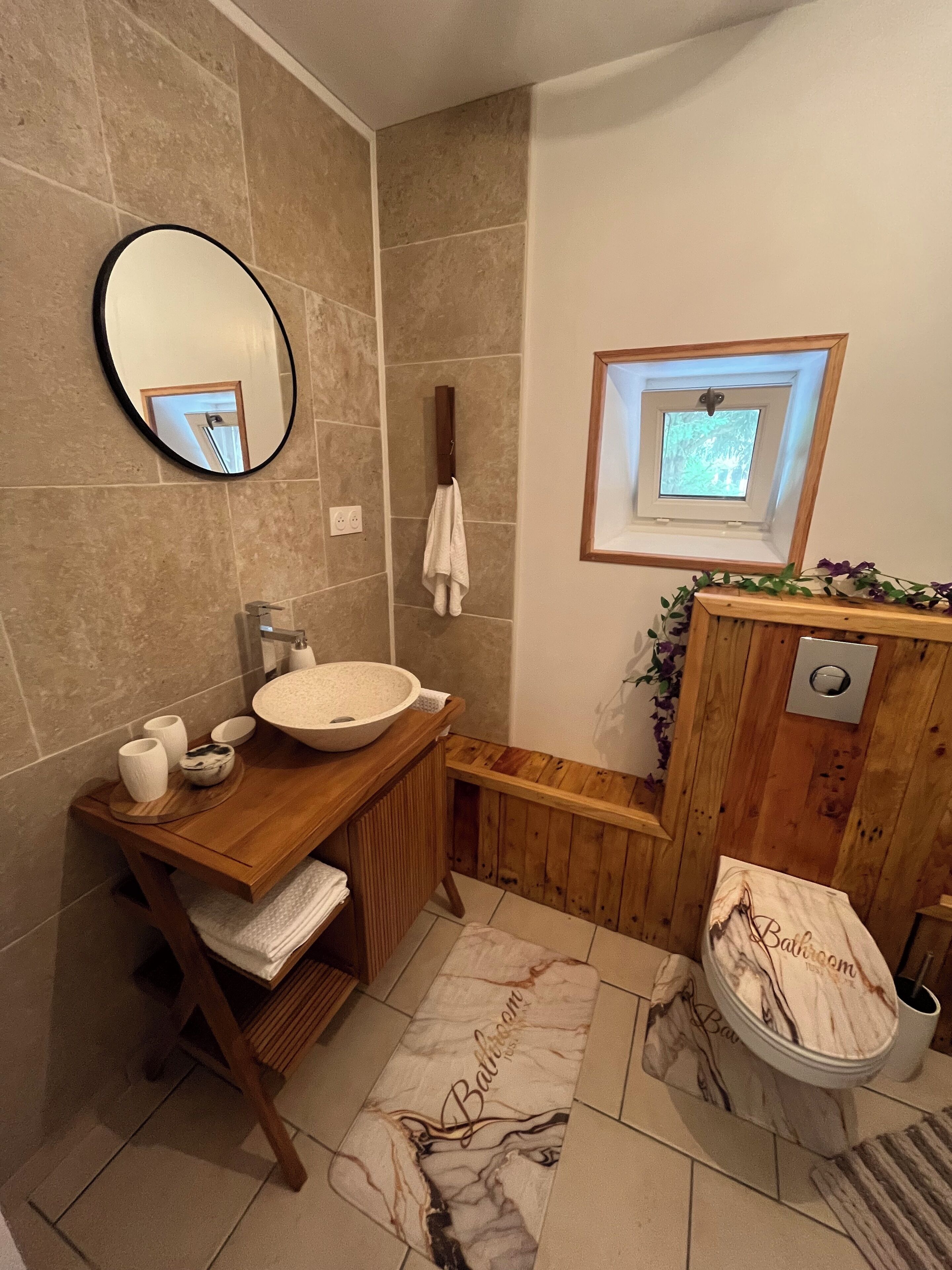 A bathroom with a wooden vanity, a large mirror, a sink, a window, and a toilet.