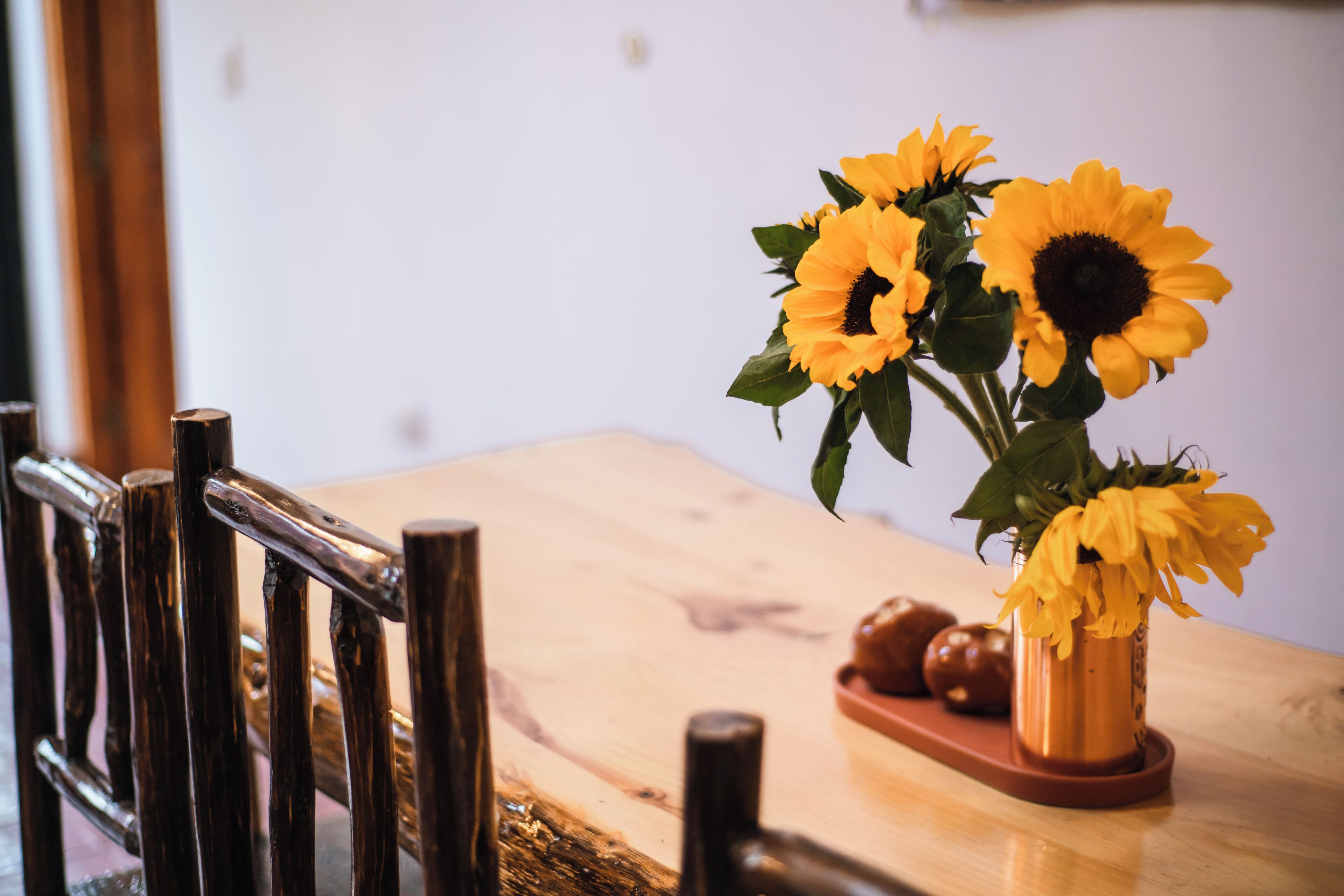 A wooden dining table with a vase of sunflowers and a wooden tray with decorative items.