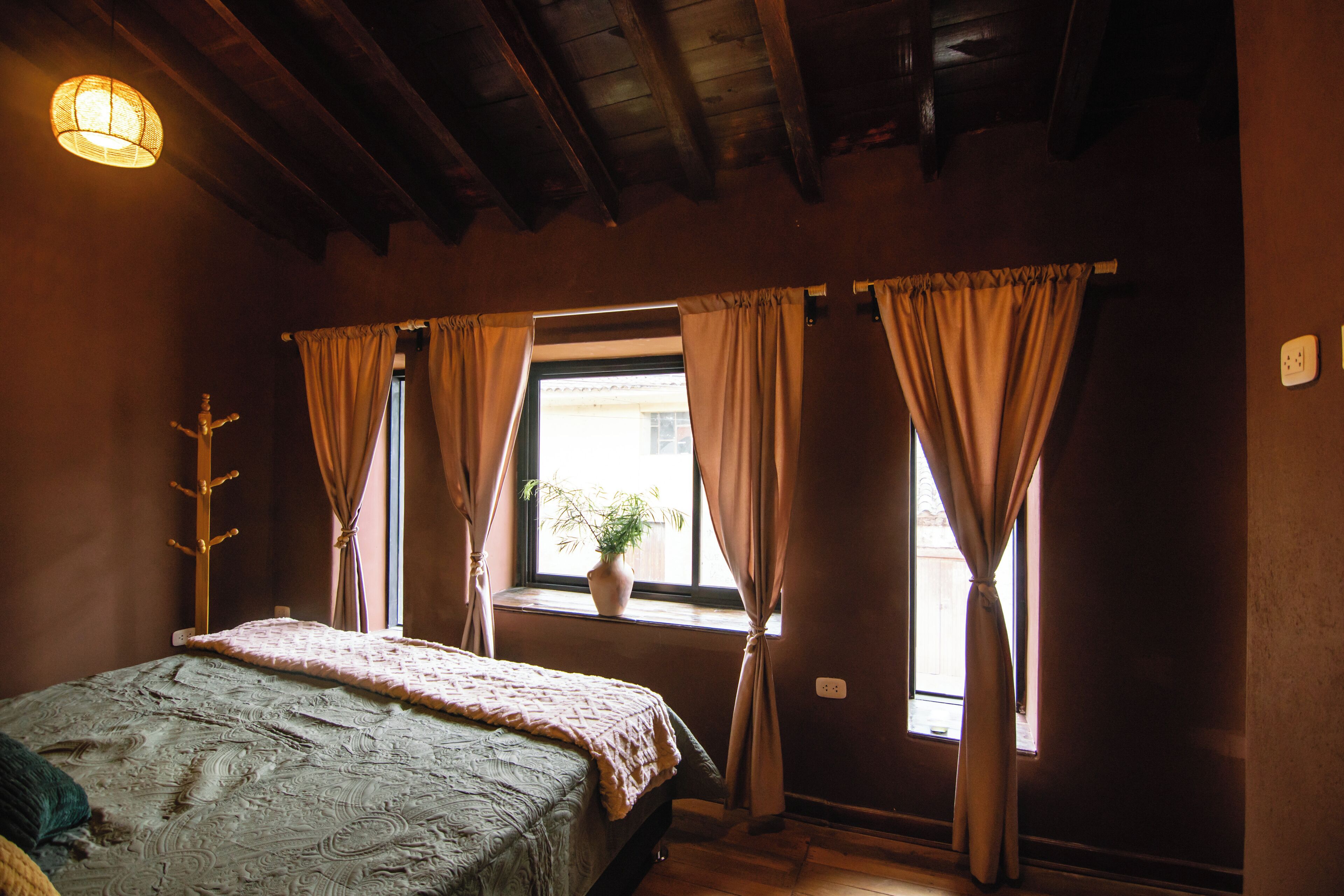 Un dormitorio con cama, una ventana con cortinas, un perchero en la pared y una lámpara en el techo.