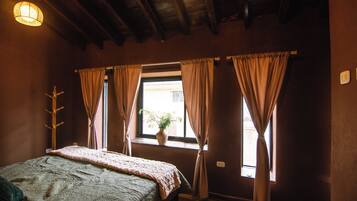 Un dormitorio con cama, una ventana con cortinas, un perchero en la pared y una lámpara en el techo.