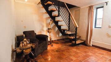A living room with a wooden staircase, a sofa, a small table with a bottle and glass, and a floor lamp.