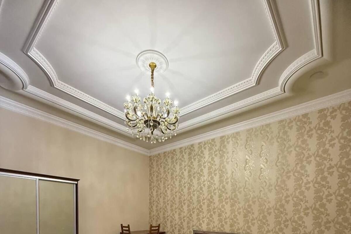 A bedroom with a large bed, a chandelier, a mirror, and a patterned carpet.