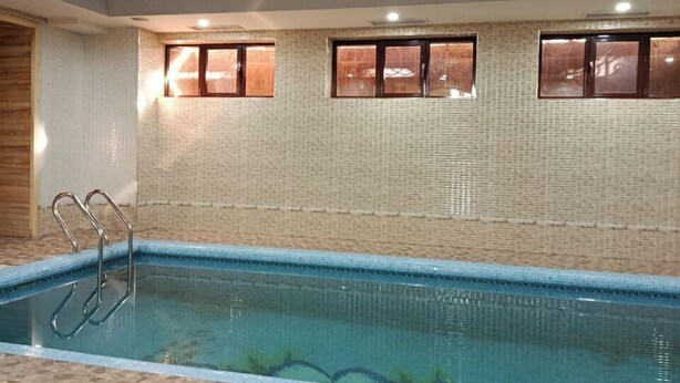 An indoor swimming pool with a tiled floor, a pool ladder, and windows with wooden frames. - Sheyx Plaza (Tashkent)