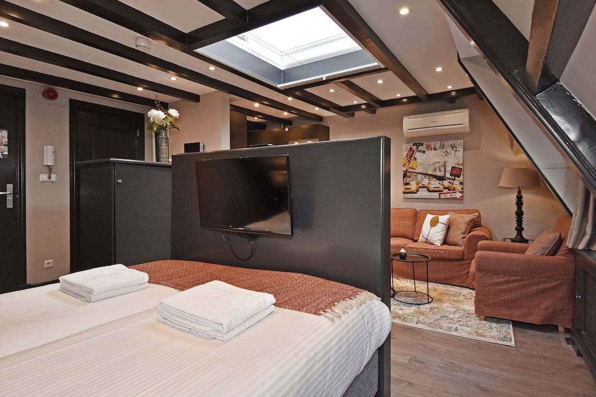 A modern hotel room with a bed, a TV, a sofa, and a staircase.